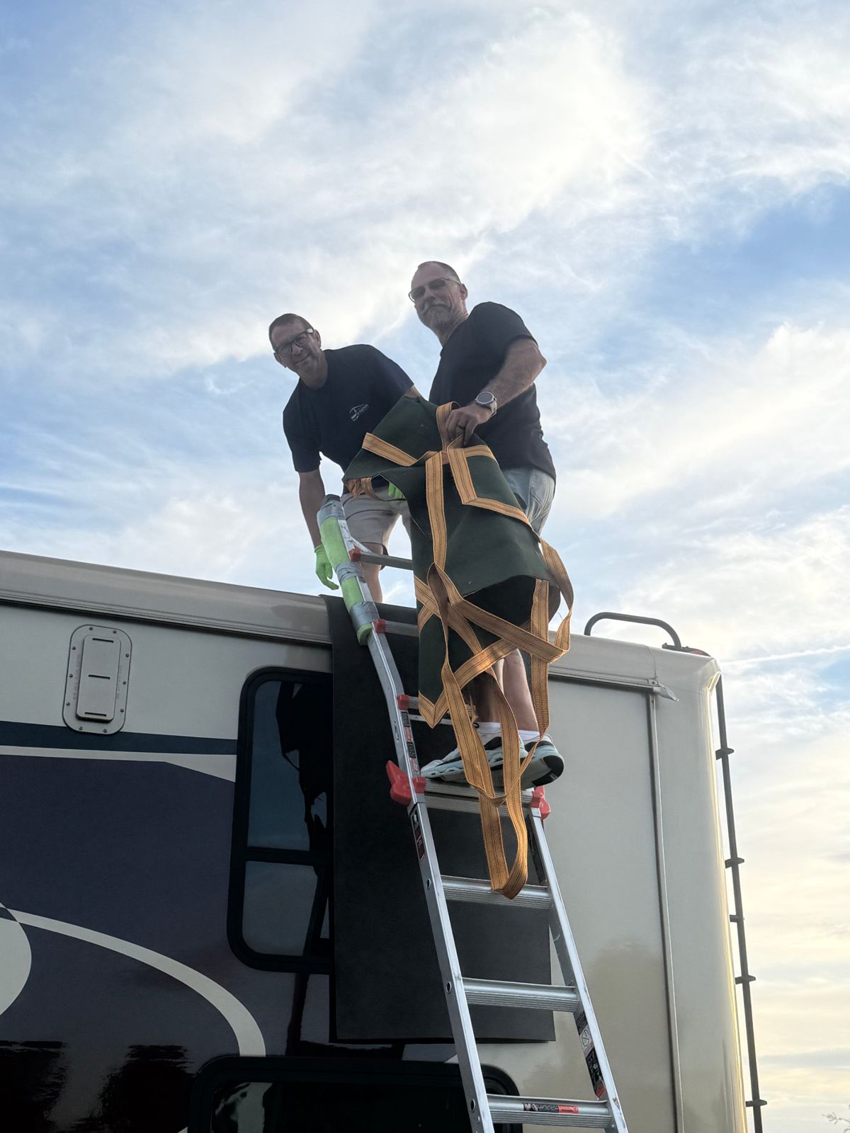 Two technicians on a ladder at the roofline of a motorhome