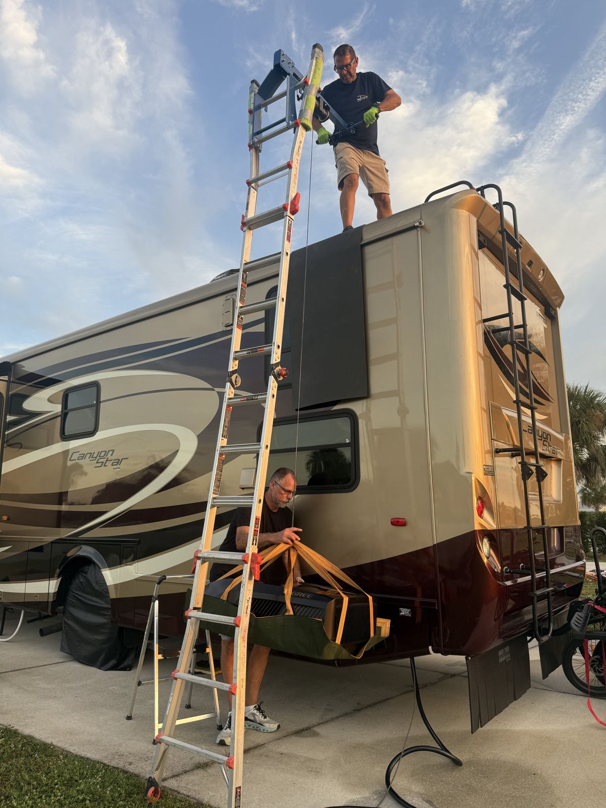Two technicians lifting a rooftop air conditioner off a motorhome