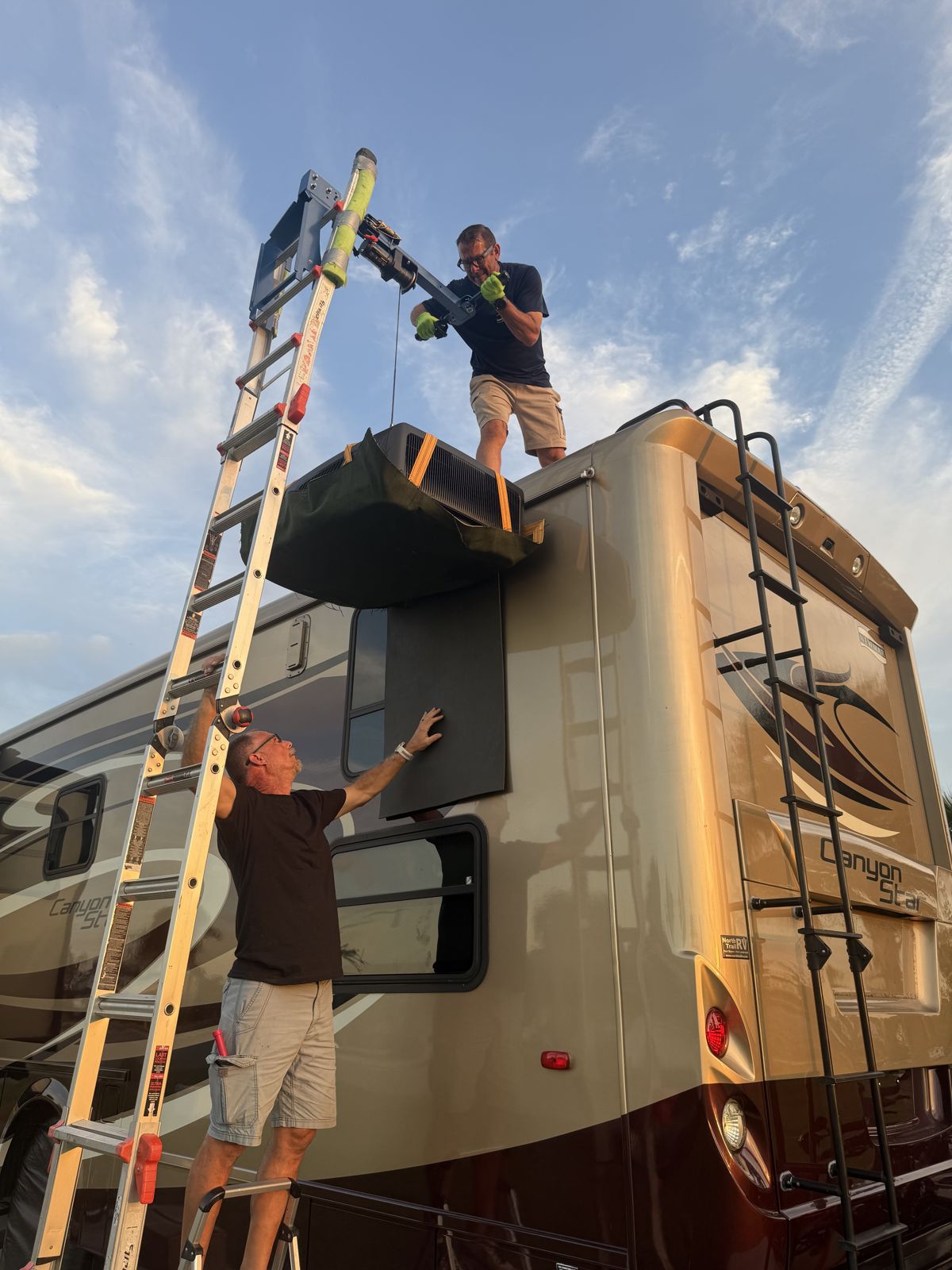 Two technicians lifting a rooftop air conditioner with a ladder hoist